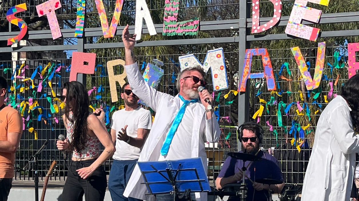 La banda de la Primavera con disfraces de estudiantes, con colorido cartel detrás.