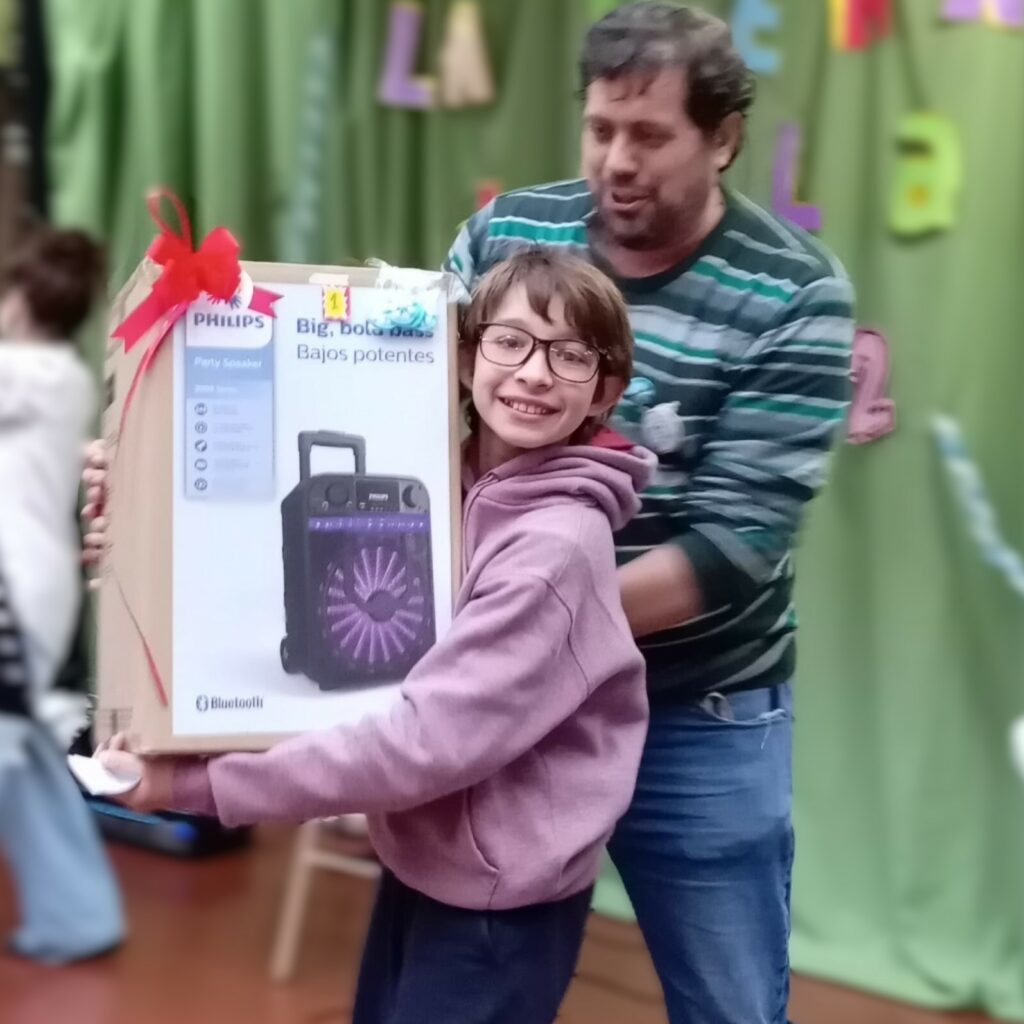 Niño feliz, sostiene una caja del tamaño de su torso, ayudado por un adulto.