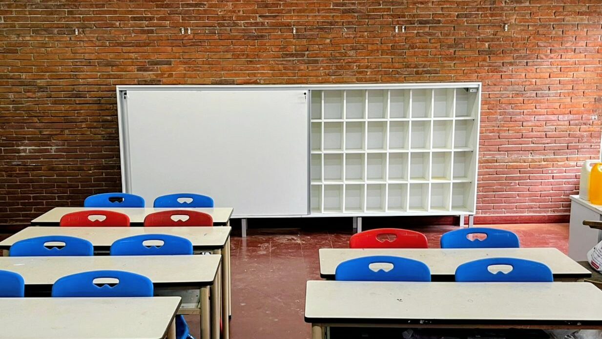 Los armarios nuevos son de melamina, apoyados en el piso, la puerta derecha está abierta y se ven los casilleros individuales para cada alumno, y puertas corredizas con llave.