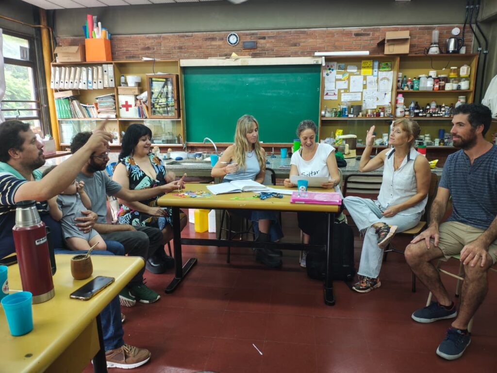 Reunión en la biblioteca de la escuela, los presenten en la asamblea discuten enérgica y amistosamente, mientras que en la mesa central la presidenta y la secretaria ordenan el acta.